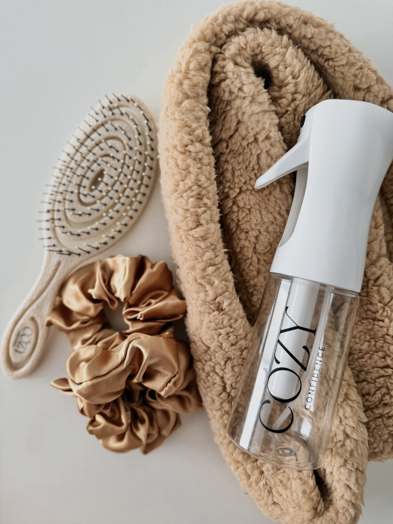 Oatmeal Curl Kit flat lay for heatless curls with a rolled camel fluffy CurlBand, gold silk scrunchies, beige Volume Brush and white Cozy Confidence spray bottle
