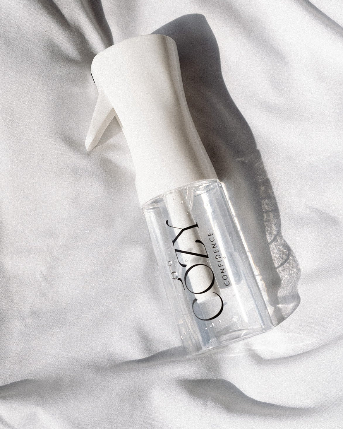 Cozy Confidence fine mist spray bottle with a white spray top on white sheets, used to lightly mist hair for heatless curls