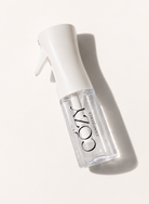 A clear spray bottle with a white spray top and trigger, featuring the brand name 'COZY CONFIDENCE' printed in black on the bottle. The bottle is photographed diagonally on a warm off-white background with a soft shadow cast to the right.