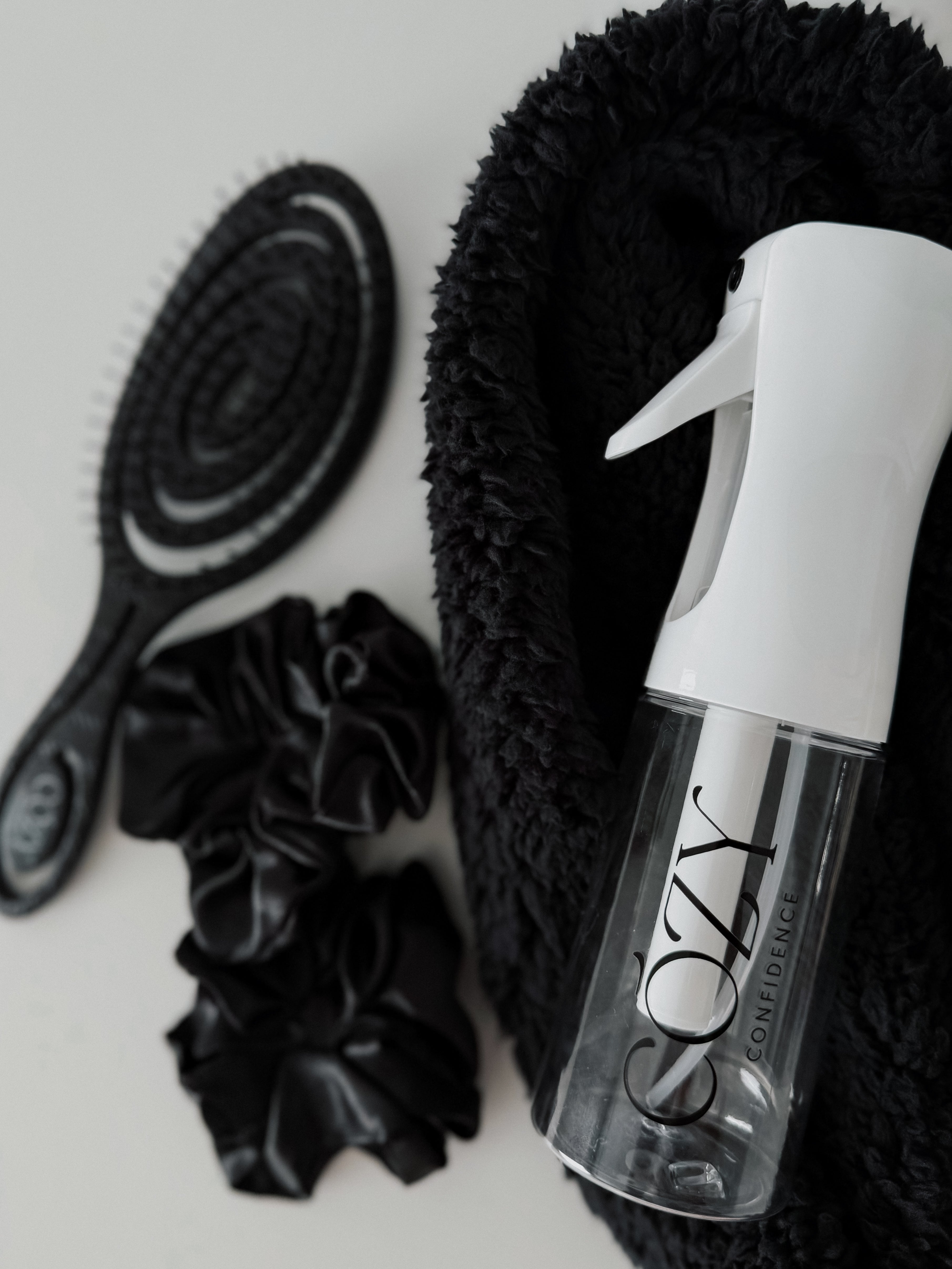 Black Curl Kit flat lay for heatless curls with a rolled black fluffy CurlBand, black silk scrunchies, black Volume Brush and white Cozy Confidence spray bottle