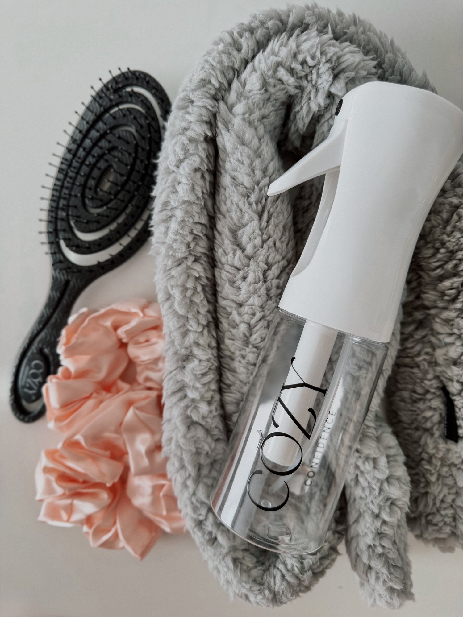 Cloud Curl Kit for heatless curls with a light gray fluffy CurlBand, blush pink silk scrunchies, black Volume Brush and white Cozy Confidence spray bottle