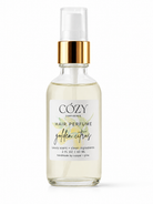 A clear glass spray bottle of Cozy Confidence Hair Perfume in the Golden Citrus scent, featuring a white label and a shiny gold collar with a clear spray top, set against a plain white background.