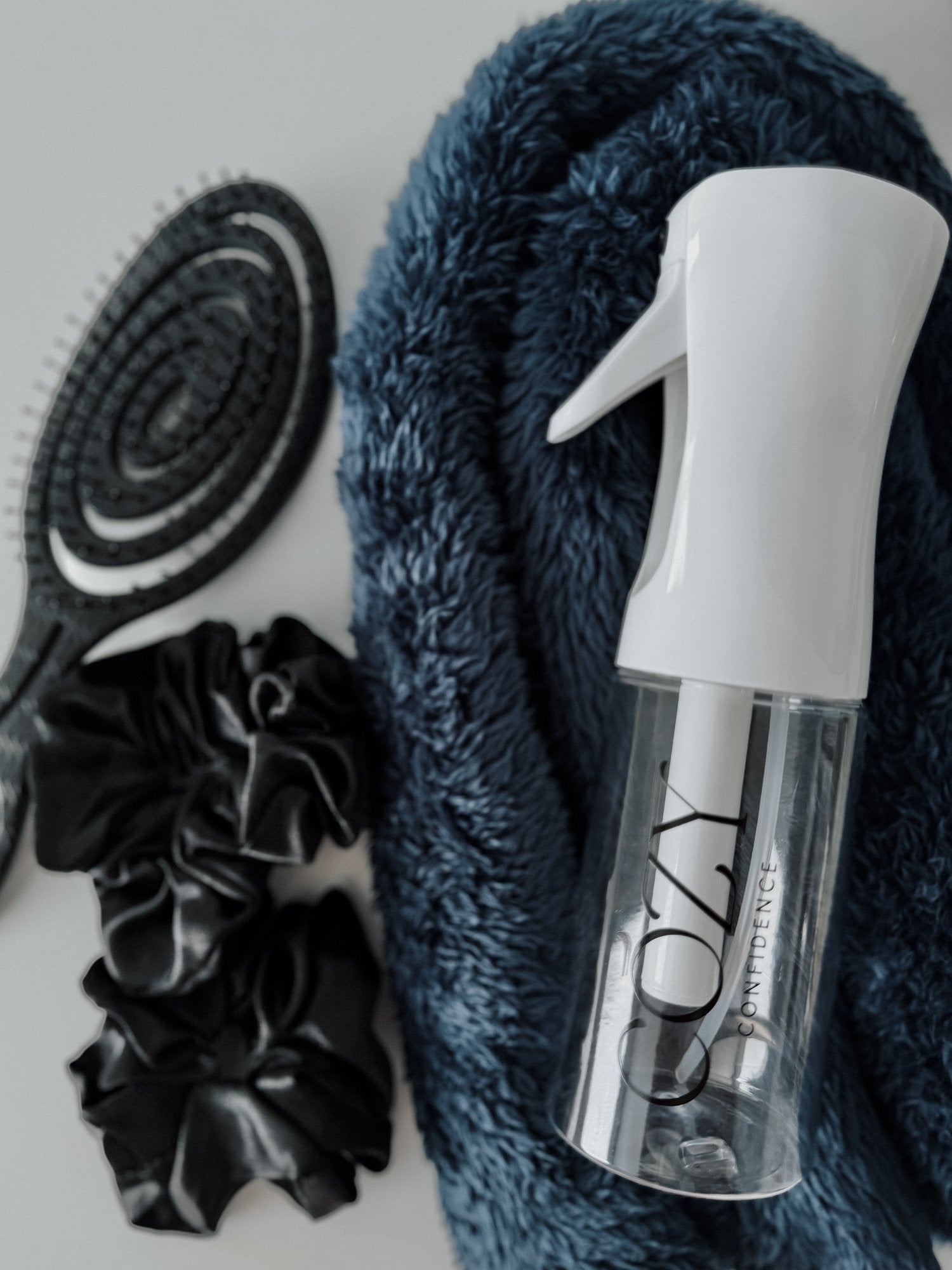 Midnight Curl Kit flat lay with a navy blue CurlBand for heatless curls, two black silk scrunchies, a black Volume Brush and a white Cozy Confidence spray bottle